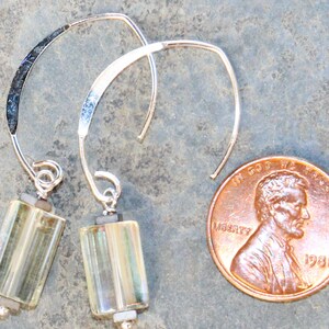 May include: A pair of silver-tone earrings with a curved design. Each earring features a rectangular, iridescent glass bead suspended from a silver wire. A U.S. penny is included for size reference.
