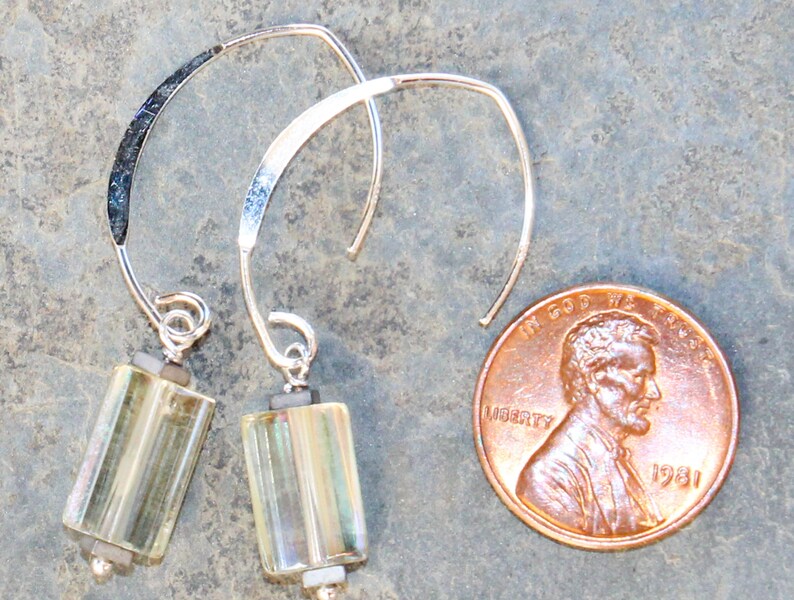 May include: A pair of silver-tone earrings with a curved design. Each earring features a rectangular, iridescent glass bead suspended from a silver wire. A U.S. penny is included for size reference.