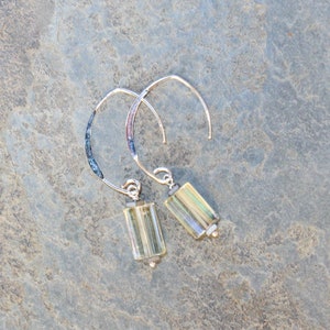May include: A pair of silver hoop earrings with rectangular, light yellow-green beads. The hoops have a curved design with a textured, dark blue and purple section near the top. The earrings are displayed on a gray, textured surface.