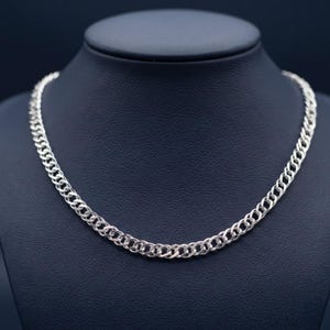 May include: A silver-toned chain necklace featuring a series of interlocking, rounded metal links. The necklace has a polished, reflective surface and a consistent, repeating pattern throughout the entire length of the chain, creating a uniform look.