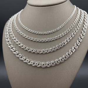 May include: Four silver-toned double curb chain necklaces displayed in a nested arrangement. Each chain features a repeating pattern of interlocking oval links with a polished metallic finish, graduating in thickness from the innermost to the outermost.