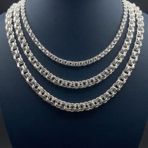 Puede incluir: Un conjunto de tres collares de tono plateado con un diseño de eslabones redondos entrelazados. Cada collar muestra un patrón circular consistente con un acabado metálico pulido, dispuesto en una formación anidada de menor a mayor.