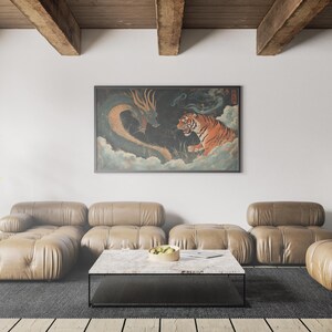 K&ouml;nnte beinhalten: Ein braunes Ledersofa in L-Form mit einem schwarzen Couchtisch davor. Ein gerahmtes Bild eines Tigers und eines Drachen in einer Wolkenlandschaft h&auml;ngt an der Wand hinter dem Sofa. Eine Lampe mit einem klaren Glasschirm steht auf einem schwarzen Beistelltisch rechts neben dem Sofa.