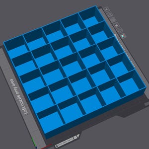 May include: A blue, rectangular 3D-printed organizer with multiple square compartments. The text "Left nozzle only area" and "Right nozzle only area" are visible. The organizer is on a gray surface.