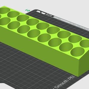 Puede incluir: Un objeto rectangular verde brillante con 18 agujeros circulares espaciados uniformemente. El objeto está sobre una superficie negra con un patrón de cuadrícula. El diseño parece ser un artículo impreso en 3D, posiblemente un contenedor de almacenamiento o un organizador.