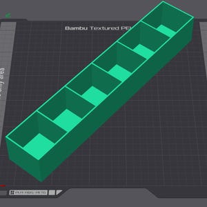Könnte beinhalten: Ein 3D-gerenderter, grüner rechteckiger Organizer mit fünf Fächern. Der Text "Bambu Textured PE" ist sichtbar. Der Organizer befindet sich auf einer dunkelgrauen Oberfläche mit Text, der "Left nozzle only area" und "Right nozzle only area" anzeigt.