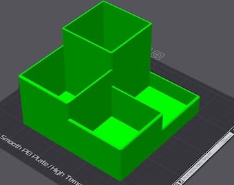 May include: A bright green, 3D-printed desk organizer with multiple compartments. The design features a tall, square section and two lower, rectangular sections. The organizer sits on a dark gray surface.
