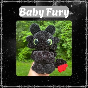May include: A black plush dragon with large green eyes and a red paw. The dragon is made of a soft, textured material. The text "Baby Fury" is displayed above the dragon in a white font.