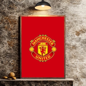 Op de afbeelding: Ingelijste poster met het Manchester United-logo op een rode achtergrond. Het logo, in geel en rood, toont de woorden "Manchester United" rond een wapen met een schip en duivel.