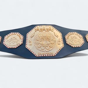 May include: A championship belt with a navy blue strap and gold-colored metal plates. The central plate features a sun-like design with the word "CAMPEON" below. Smaller plates on each side have text and a world map.