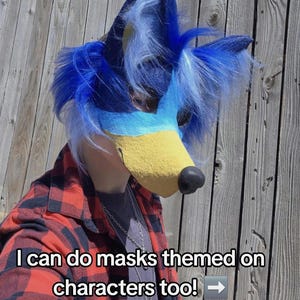 May include: A blue and yellow furry mask with a black nose and blue fur accents. The mask is worn with a red and black plaid shirt. Text on the image reads, "I can do masks themed on characters too!"