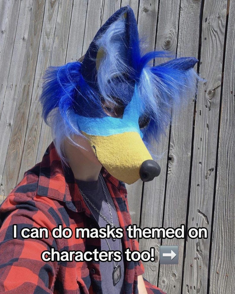 May include: A blue and yellow furry mask with a black nose and blue fur accents. The mask is worn with a red and black plaid shirt. Text on the image reads, "I can do masks themed on characters too!"