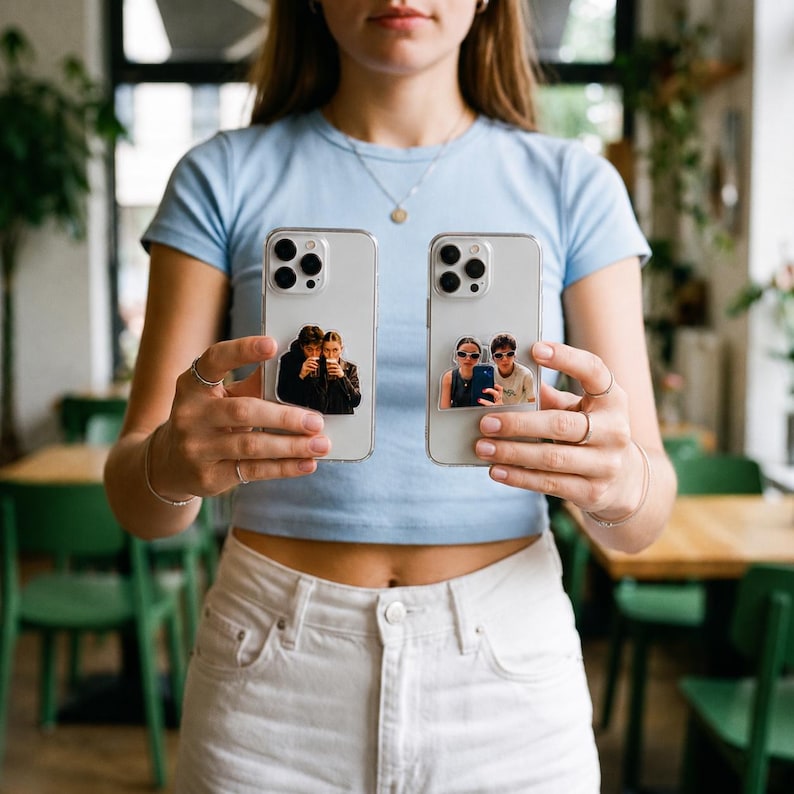 May include: Two clear smartphone cases, each featuring a unique photographic sticker on the back. The left case displays a sticker of two people holding drinks, while the right case features a sticker of two people wearing sunglasses and taking a photo.