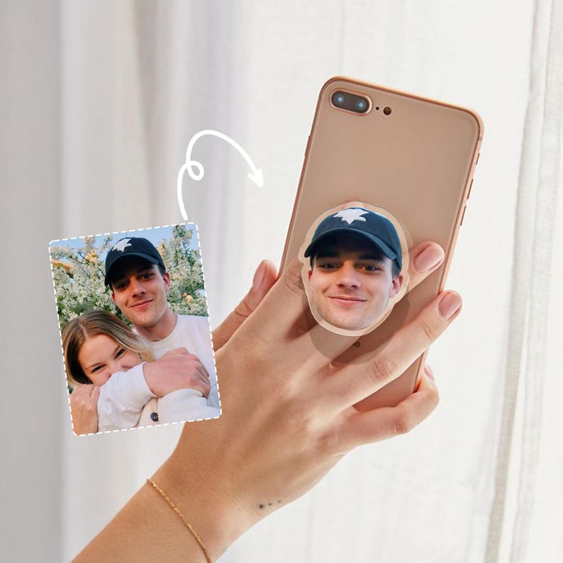 May include: A gold smartphone with a custom phone grip featuring a photo of a person wearing a black baseball cap. The phone grip is a round sticker with a white border.