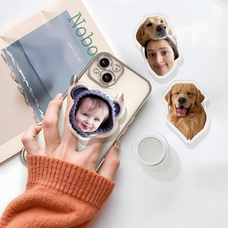 May include: A white iPhone case with a clear back. A sticker of a baby wearing a blue and grey hooded sweater is on the back of the case. There are two other stickers on a white surface: one of a golden retriever and one of a woman with a golden retriever on her head.