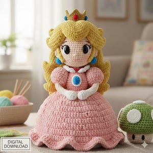 May include: A crocheted Princess Peach doll in a pink dress, with blonde hair and a gold crown. The doll has blue earrings and a blue and white brooch. A green mushroom with white spots is next to the doll. The words "DIGITAL DOWNLOAD" are in the bottom left corner.