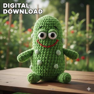 May include: A green crocheted pickle character with white accents and a smiling red mouth. The text "DIGITAL DOWNLOAD" is at the top. The pickle has arms and feet and is sitting on a wooden surface.