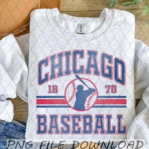 May include: A light gray sweatshirt with a distressed Chicago Baseball design. The design features the word "CHICAGO" in blue, the years "18" and "70", and the word "BASEBALL" in blue. A baseball and batter silhouette are in the center.
