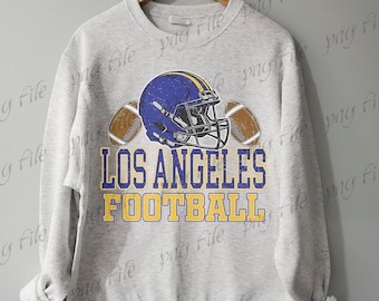 Op de afbeelding: Een lichtgrijs sweatshirt met een blauw en gele footballhelm en twee voetballen. De tekst "LOS ANGELES FOOTBALL" is gedrukt in blauw en geel. Het sweatshirt hangt aan een houten hanger.