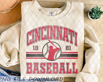 Op de afbeelding: Crèmekleurige sweatshirt met de tekst "CINCINNATI BASEBALL" in het rood en een honkbalafbeelding. Het ontwerp bevat de nummers "18" en "81". De sweatshirt heeft een ronde hals en lange mouwen.