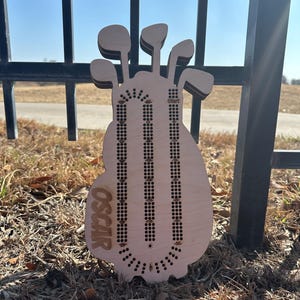 K&ouml;nnte beinhalten: Ein h&ouml;lzernes Cribbage-Brett in Form einer Golftasche mit Golfschl&auml;gern oben. Das Brett hat drei Bahnen f&uuml;r die Stifte und der Name "OSCAR" ist auf der Vorderseite eingraviert. Das Brett ist aus hellem Holz gefertigt.