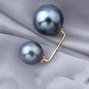 Peut inclure: Une broche en or avec deux perles gris foncé. Les perles sont attachées à une barre en or qui est pliée à un angle de 90 degrés.
