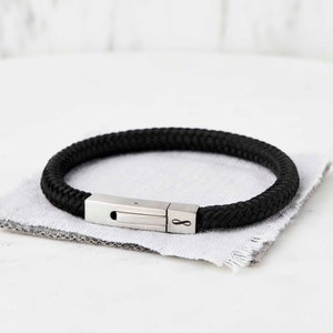 Op de afbeelding: Een zwarte gevlochten leren armband met een zilveren sluiting met een oneindigheidssymbool.