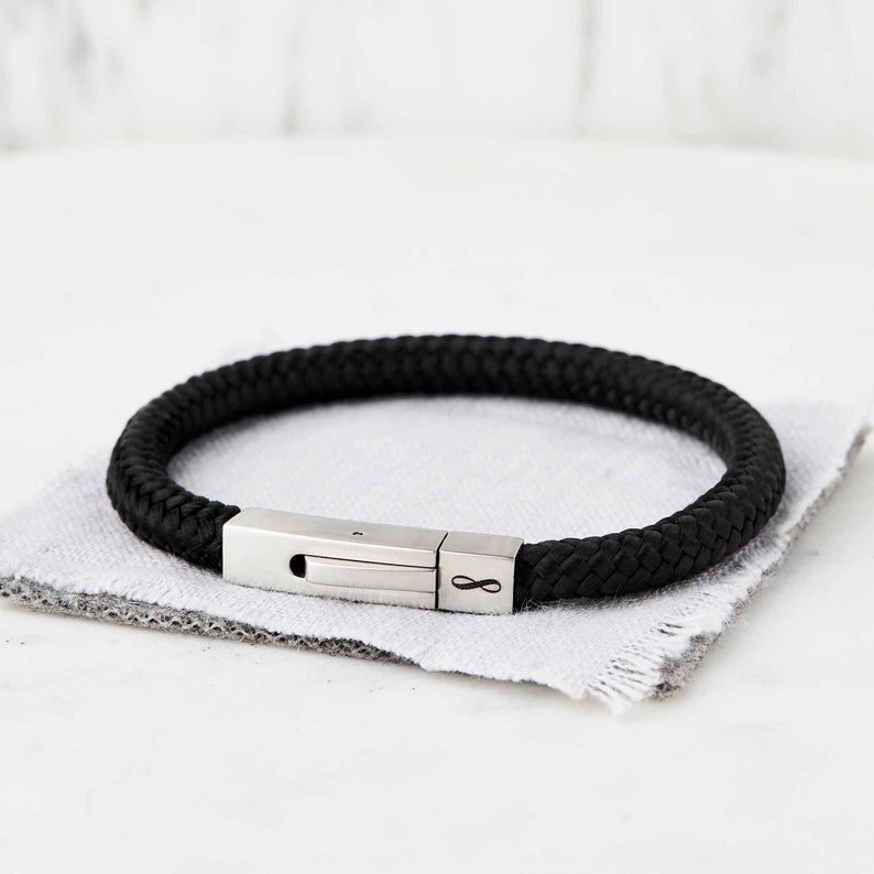 Op de afbeelding: Een zwarte gevlochten leren armband met een zilveren sluiting met een oneindigheidssymbool.