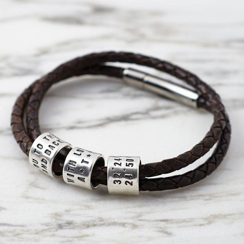 May include: A brown leather bracelet with silver beads. The beads are engraved with the words "To the land back with love a t*" and the numbers "32.24 24.50".