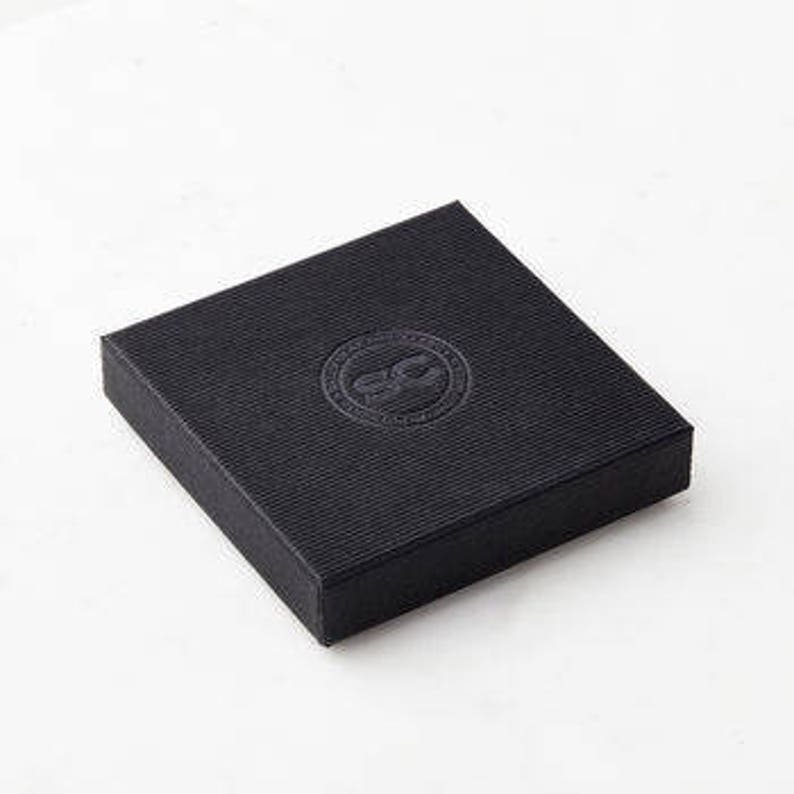 May include: A black square box with a raised, circular logo in the centre. The logo is a stylised letter "C" inside a circle.
