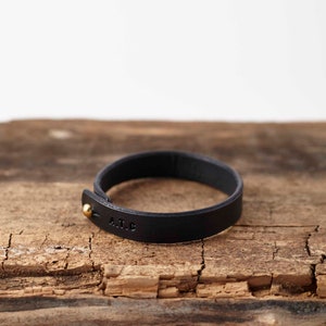 Peut inclure: Un bracelet en cuir noir avec un fermoir en or et les initiales "A.I.C." grav&eacute;es sur la bande.