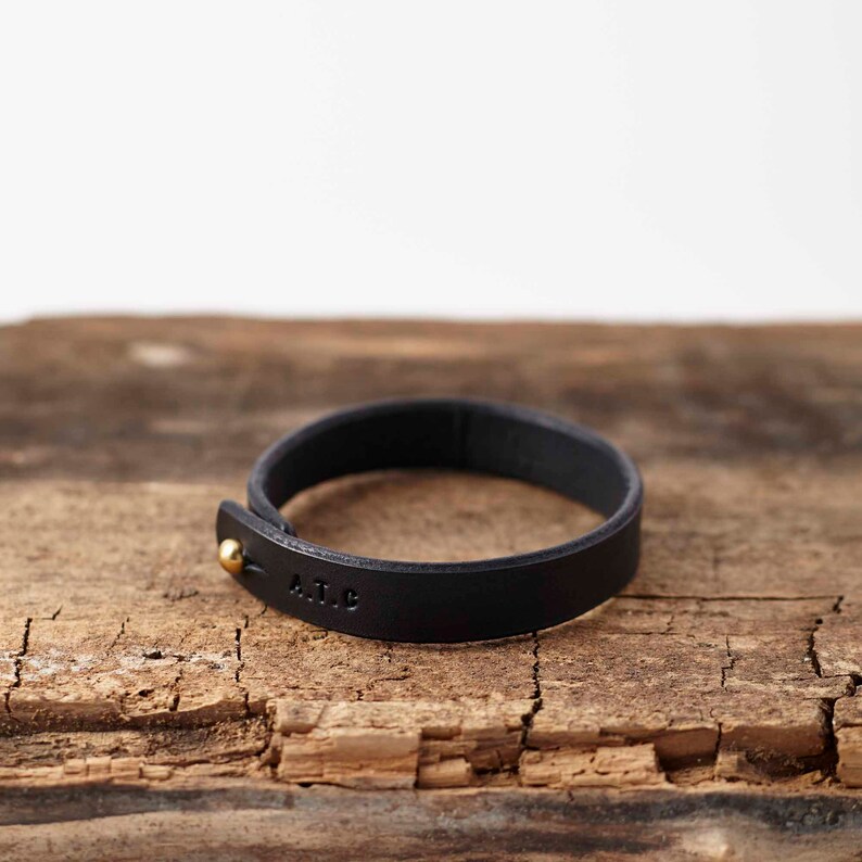 Peut inclure: Un bracelet en cuir noir avec un fermoir en or et les initiales "A.I.C." grav&eacute;es sur la bande.