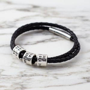 Puede incluir: Un brazalete de cuero negro con un dise&ntilde;o trenzado y cuatro cuentas de plata. Las cuentas est&aacute;n grabadas con el texto "54.08.02.32", "ARTHUR & WILL", "LOVE YOU" y "XXXX".
