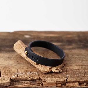 Peut inclure: Un bracelet en cuir noir avec un fermoir en or et les initiales "A.T.C." grav&eacute;es.