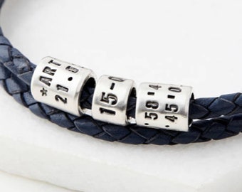 May include: A navy blue leather bracelet with silver beads. The beads are engraved with the text "*ART 21.8", "15-0", and ".58.14 .45.10".