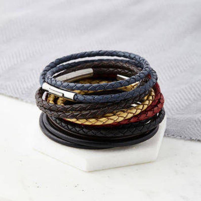 May include: A stack of braided leather bracelets in various colours, including black, brown, blue, red, and gold. The bracelets have a silver clasp.