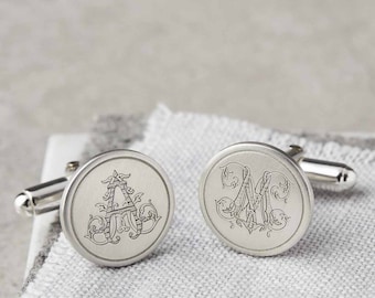 Puede incluir: Un par de gemelos de plata con iniciales grabadas. Los gemelos son redondos y tienen un diseño decorativo alrededor de las iniciales.
