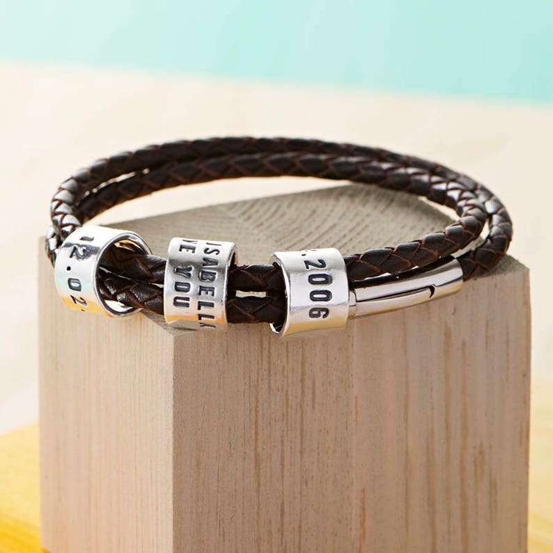 May include: A brown leather bracelet with silver beads. The beads are engraved with the words "Isabella", "Love You", "12.02", and "2006".