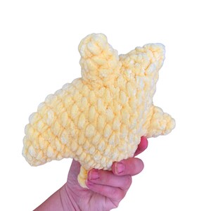 Puede incluir: Un juguete de peluche de color amarillo p&aacute;lido con forma de estrella de cinco puntas, elaborado con hilo grueso y texturizado con un aspecto esponjoso y rizado. La estrella presenta puntas redondeadas y una construcci&oacute;n densa y rellena.