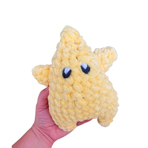 Puede incluir: Un peluche con forma de estrella de color amarillo p&aacute;lido hecho de hilo grueso y suave. El peluche presenta un dise&ntilde;o de cinco puntas con dos peque&ntilde;os ojos bordados que consisten en pupilas azul oscuro y reflejos blancos, d&aacute;ndole un aspecto sencillo.