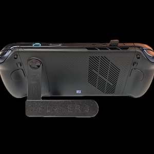 May include: A black handheld gaming console featuring a rear-facing kickstand with the text XPLAYER 3 embossed on the surface. The device includes a prominent ventilation grille on the back, shoulder buttons, and a power button with a blue light.
