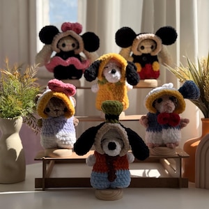Puede incluir: Una colección de seis pequeñas muñecas de ganchillo hechas a mano, inspiradas en personajes de dibujos animados clásicos. Cada muñeca lleva una capucha o sombrero único y extraíble, con esquemas de colores como negro, amarillo, rojo, azul y rosa, exhibidas en un soporte escalonado.
