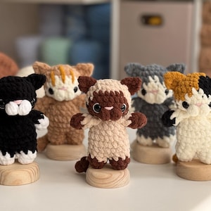 Puede incluir: Colecci&oacute;n de cinco figuras de gato de ganchillo hechas a mano en varios colores, incluyendo negro, marr&oacute;n, gris y carey. Cada gato est&aacute; montado sobre una peque&ntilde;a base de madera. Los gatos tienen detalles y est&aacute;n de pie con los brazos extendidos.