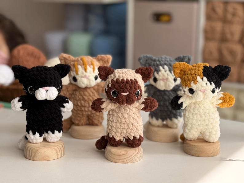 Puede incluir: Colecci&oacute;n de cinco figuras de gato de ganchillo hechas a mano en varios colores, incluyendo negro, marr&oacute;n, gris y carey. Cada gato est&aacute; montado sobre una peque&ntilde;a base de madera. Los gatos tienen detalles y est&aacute;n de pie con los brazos extendidos.