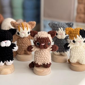 Puede incluir: Colecci&oacute;n de seis figuras de gato de ganchillo hechas a mano en varios colores, incluyendo negro, marr&oacute;n, gris y carey. Cada gato est&aacute; montado sobre una peque&ntilde;a base de madera, mostrando sus detalles y adorables poses.