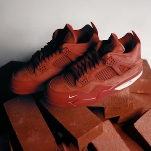 May include: A pair of red high-top sneakers with a textured design. The sneakers feature a white sole and a small white Nike logo. The shoes are placed on a pile of red bricks, creating a monochromatic theme.