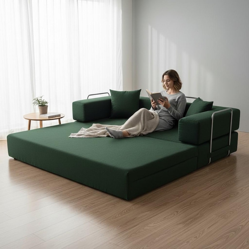 Peut inclure: Un canap&eacute;-lit vert fonc&eacute; avec des coussins et accoudoirs assortis. Le canap&eacute; est dans un cadre de salon moderne avec une personne lisant un livre. Le canap&eacute; mesure environ 200 cm de long.