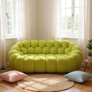 May include: A lime green, tufted sofa with a rounded shape. Two square cushions, one pink and one light blue, sit on the floor in front of the sofa, along with a round, woven rug. The room has large windows and sheer white curtains.