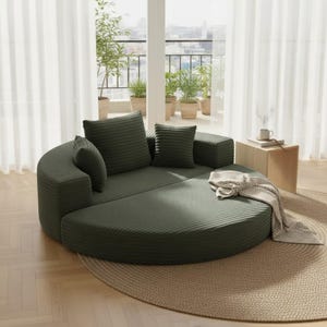 May include: A modular, olive green, round sofa with several matching throw pillows. The sofa is made of a ribbed fabric and sits on a beige rug. A small wooden side table with a mug and a blanket are also visible.