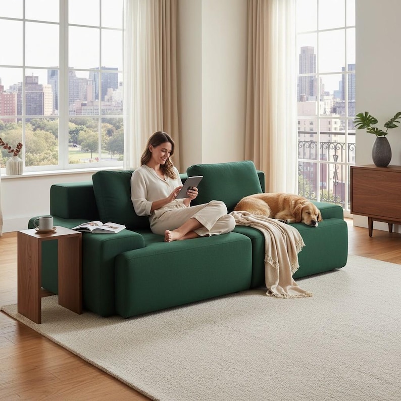 Puede incluir: Un sof&aacute; modular verde esmeralda con una mujer usando una tableta. Un perro golden retriever descansa en el sof&aacute;. Una peque&ntilde;a mesa auxiliar de madera tiene una taza y un libro. La habitaci&oacute;n tiene grandes ventanas con vistas a la ciudad.